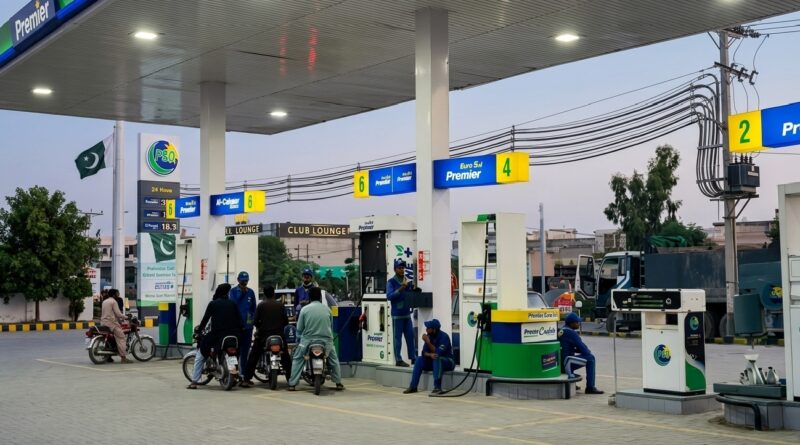 ‎A wide-angle, high-resolution shot of a modern PSO petrol station in Pakistan during twilight. The image shows several motorcyclists at the fuel pumps and attendants in blue uniforms. The station features "Euro 5 Premier" signage in blue and yellow, a large PSO pylon with a digital price board, and the Pakistani flag waving in the background. The scene is well-lit by overhead canopy lights against a soft evening sky.
